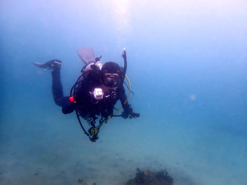 水中ライトのついたカメラを手に、青い海を泳ぐダイバー